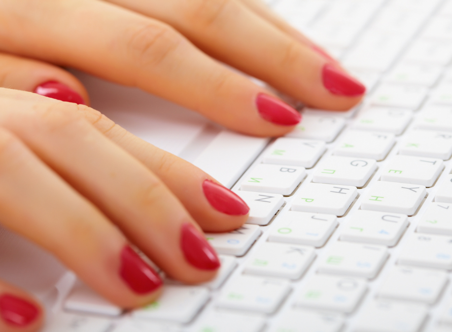 woman's hands with red nails typing on a keyboard